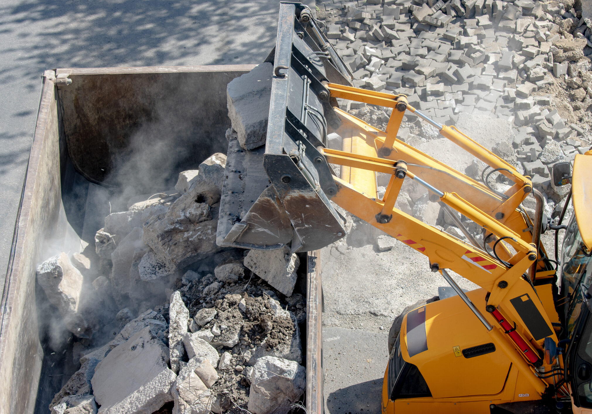 Bulldozer loader uploading concrete debris into dump truck at construction site