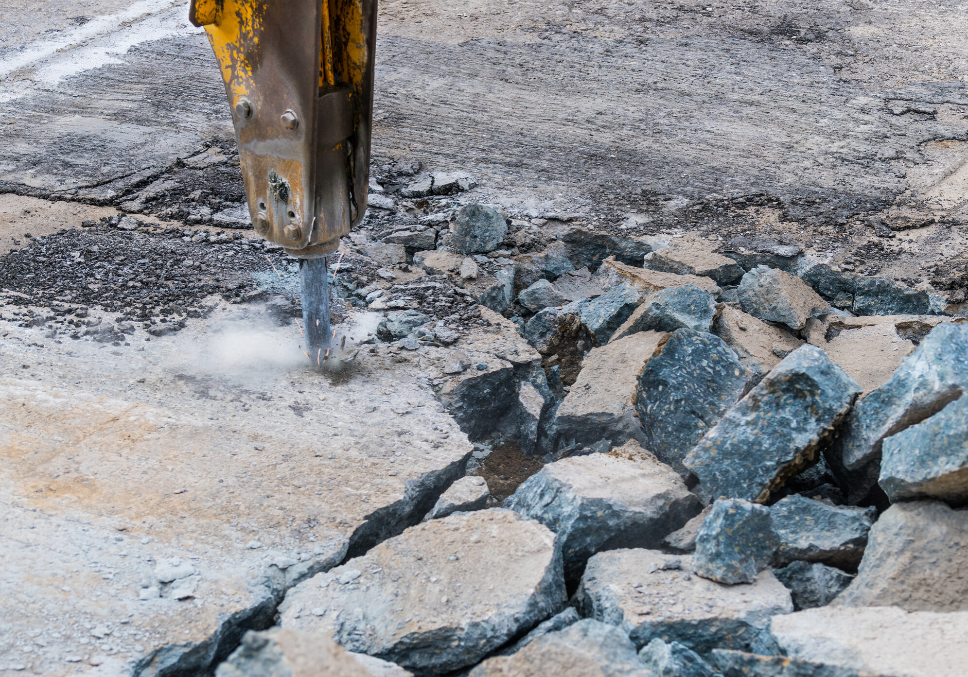 Detail of hydraulic jackhammer mounted on excavator arm working at old road reconstruction. Repairs in civil engineering