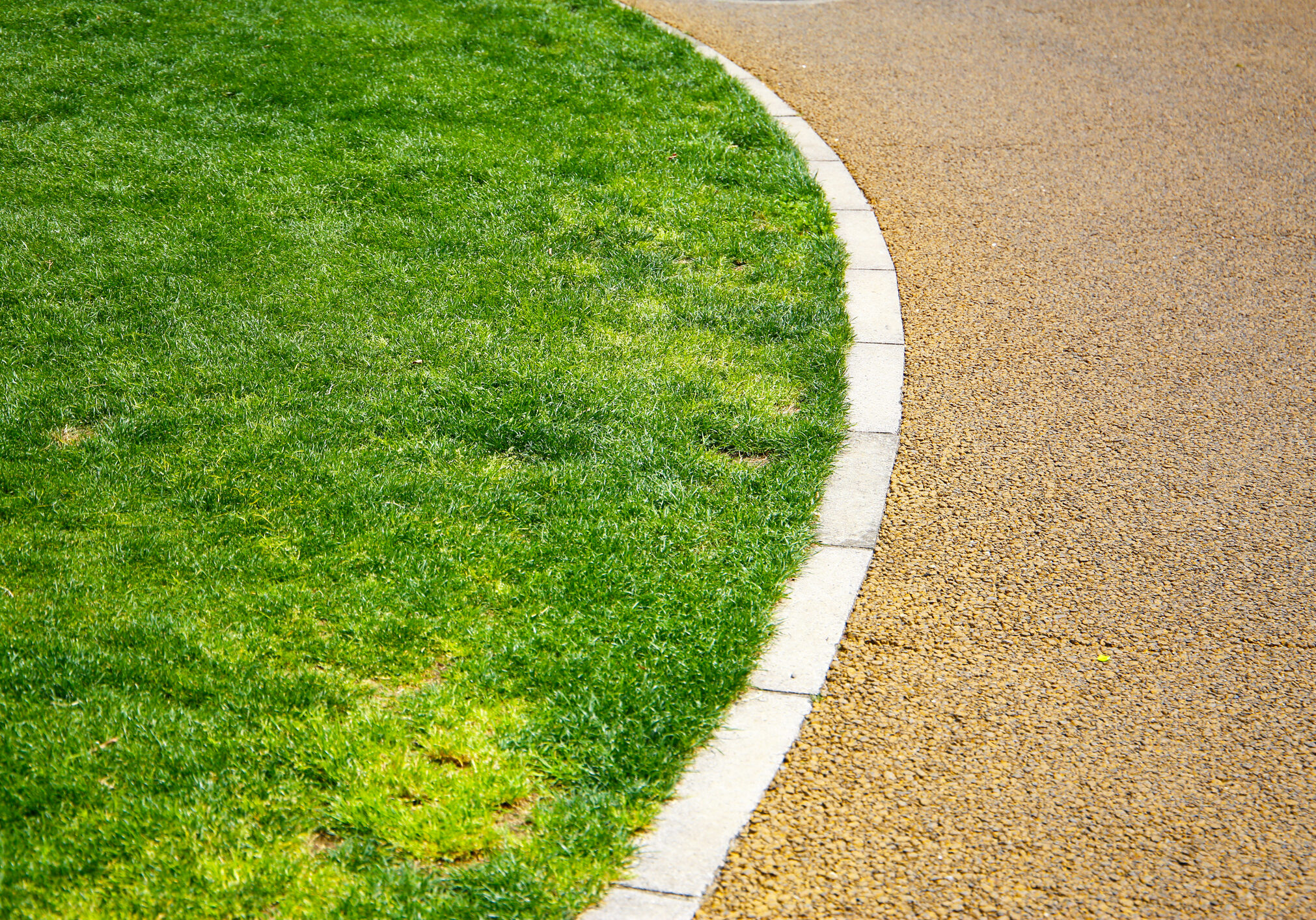 Curved pathway beside a green grassy lawn in the park.