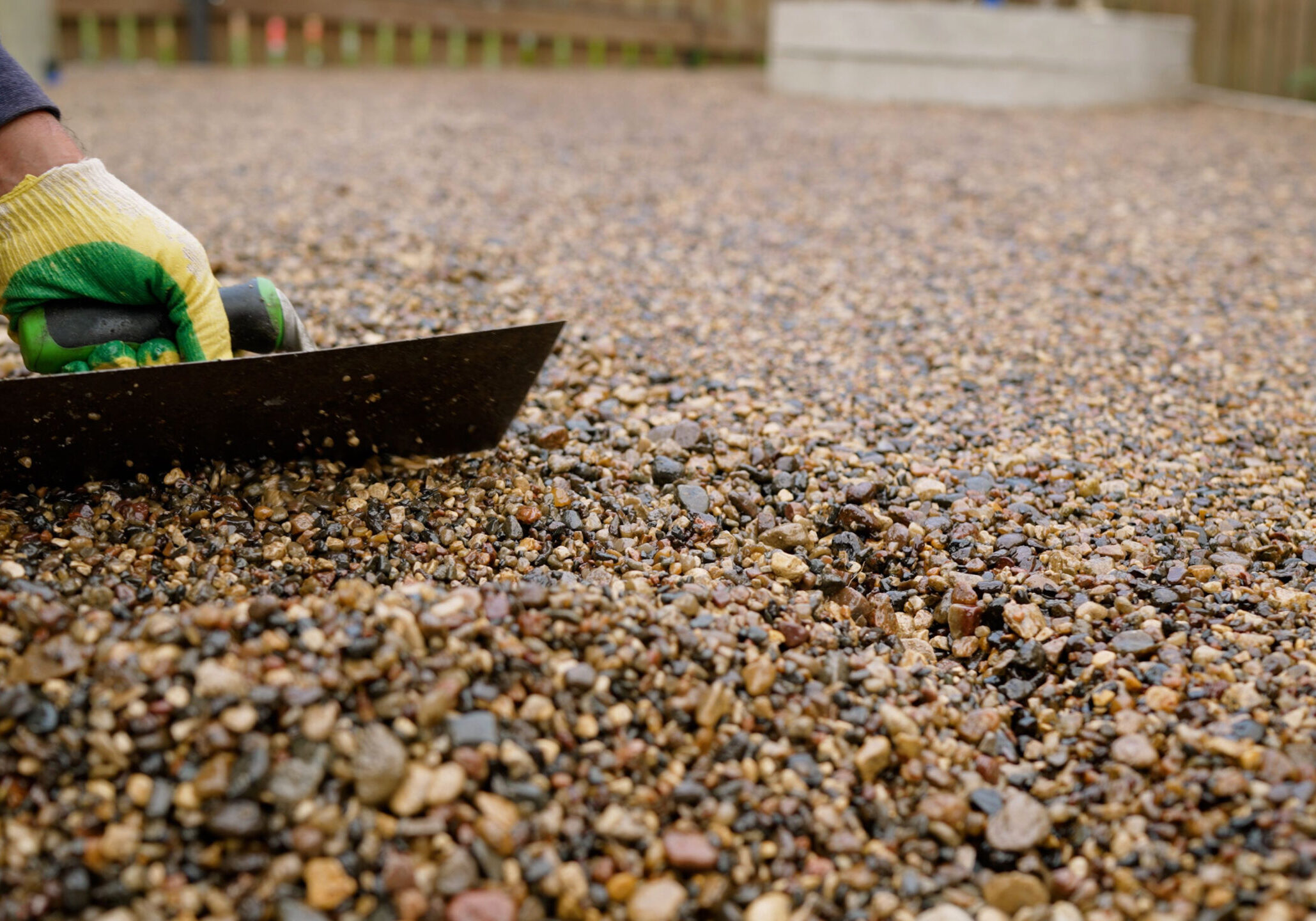 Construction worker carefully spreading gravel across concrete floor, leveling surface using professional trowel with precise manual technique